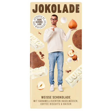 Produktverpackung (beige): JOKOLADE weiße Schokolade mit karamellisierten Haselnüssen, Coffee Biscuits & Baiser. Joko Winterscheidt steht in der Mitte mit einer Nuss auf der Hand, auf welche er mit der Anderen zeigt. Die Zutaten sind im Hintergrund zu sehen. Button: Approved by Joko Winterscheidt (Faire Schokolade)