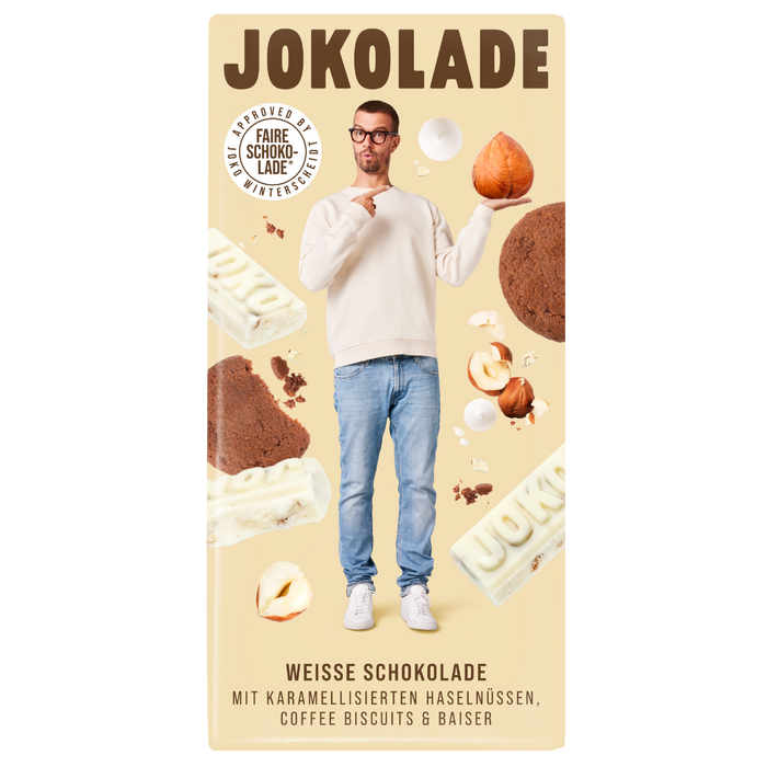 Produktverpackung (beige): JOKOLADE weiße Schokolade mit karamellisierten Haselnüssen, Coffee Biscuits & Baiser. Joko Winterscheidt steht in der Mitte mit einer Nuss auf der Hand, auf welche er mit der Anderen zeigt. Die Zutaten sind im Hintergrund zu sehen. Button: Approved by Joko Winterscheidt (Faire Schokolade)